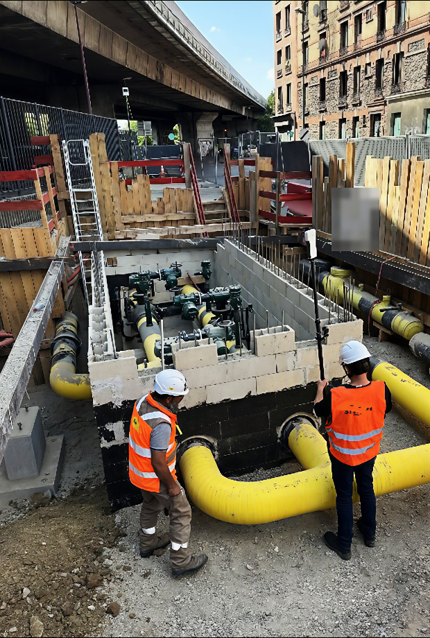 Deux techniciens au bord d’une fouille où passent des canalisations de gaz jaunes ; l’un tient une canne surmontée du tag e-Nails.